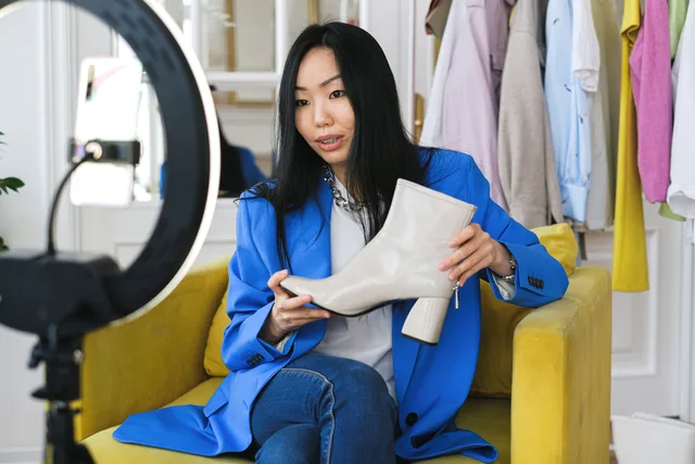 Fashion influencer streaming online reviewing shoes with smartphone and lighting ring. Creator-Inhalte im Social Commerce