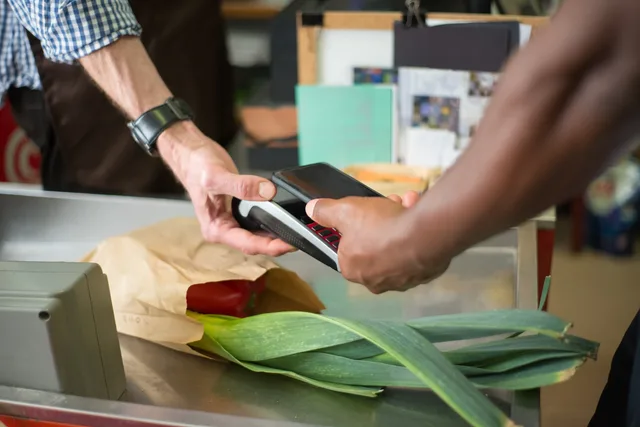 A customer making a contactless payment with a smartphone at a grocery store checkout counter. Mobile Kaufwege verbessern